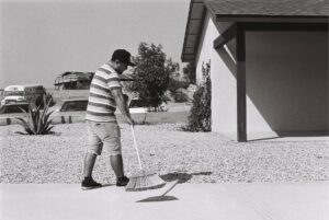 grayscale photo of man sweeping driveway